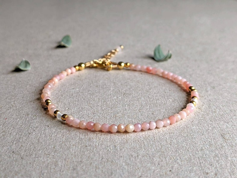 May include: A delicate pink opal gemstone bracelet with gold accents. The bracelet is made of small, round beads and has a simple, elegant design.