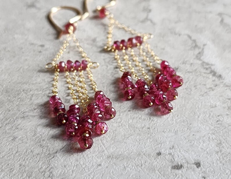 Puede incluir: Pendientes de oro con m&uacute;ltiples cadenas de peque&ntilde;as piedras preciosas rosas.