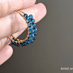 May include: Gold wire hoop earrings with blue gemstone beads. The earrings are handmade and feature a cluster of small, round blue gemstones.