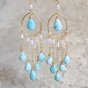 May include: Gold-tone chandelier earrings with teardrop-shaped, light blue gemstones and small white pearls. The earrings have a delicate chain design and are suspended from gold-tone hooks.