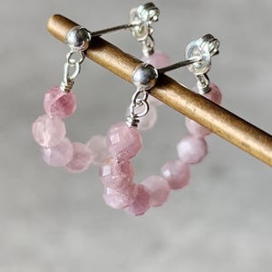 May include: A pair of silver hoop earrings with pink gemstone beads. The earrings are hanging from a wooden display stand.