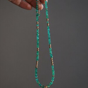 May include: A delicate gold chain necklace with green gemstone beads. The necklace is made of small, round beads that are strung together to create a simple and elegant design.