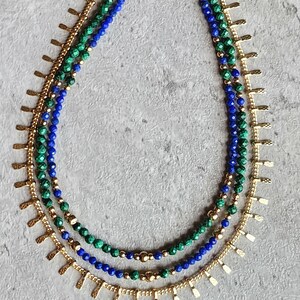 May include: A layered necklace with blue and green gemstone beads and gold accents. The necklace features a delicate chain with small, pointed gold charms.