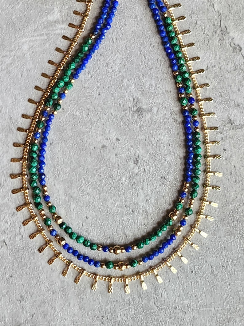 May include: A layered necklace with blue and green gemstone beads and gold accents. The necklace features a delicate chain with small, pointed gold charms.