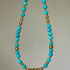 May include: A turquoise and gold beaded necklace with a cluster of gold beads in the center.