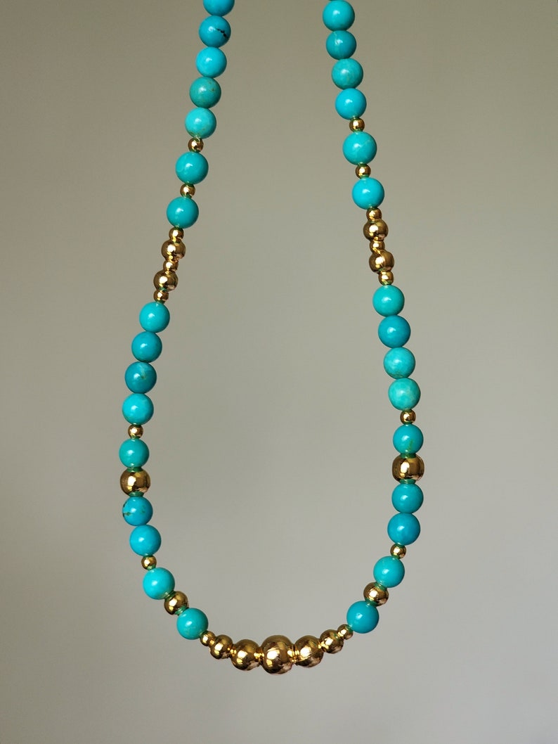 May include: A turquoise and gold beaded necklace with a cluster of gold beads in the center.