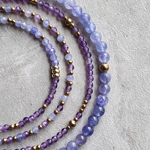 May include: A set of four bracelets featuring amethyst and blue chalcedony beads with gold accents.
