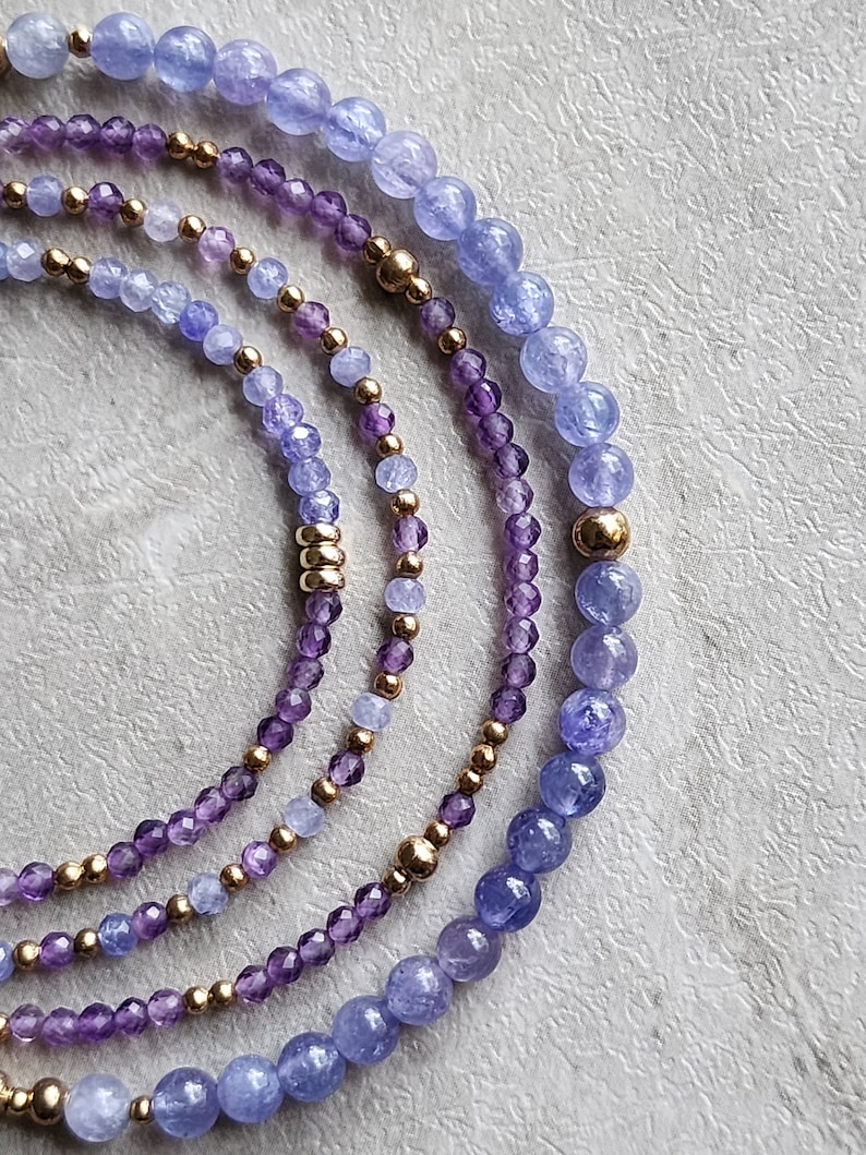 May include: A set of four bracelets featuring amethyst and blue chalcedony beads with gold accents.
