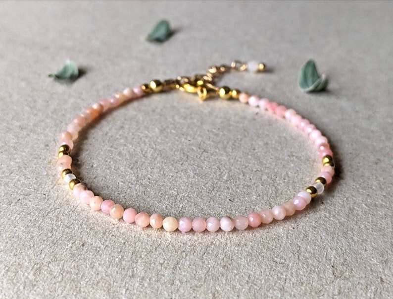 May include: A delicate pink opal gemstone bracelet with gold accents. The bracelet is made with small, round beads and has a simple, elegant design.