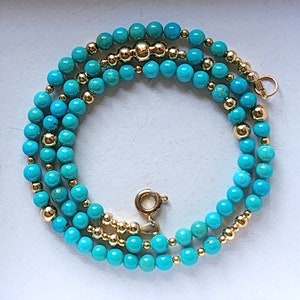 May include: A turquoise and gold beaded necklace with a clasp closure. The necklace is made of round turquoise beads and gold beads.