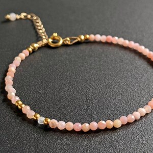 May include: A delicate pink opal gemstone bracelet with gold accents. The bracelet is made with small, faceted opal beads and gold spacer beads. The clasp is a gold lobster claw.