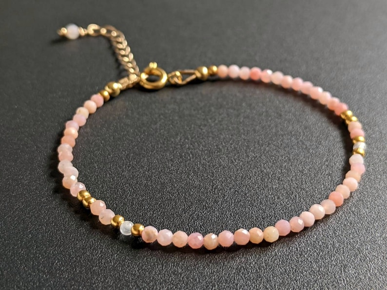 May include: A delicate pink opal gemstone bracelet with gold accents. The bracelet is made with small, faceted opal beads and gold spacer beads. The clasp is a gold lobster claw.