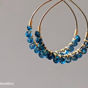 May include: Gold hoop earrings with blue gemstone beads. The earrings are made of wire and have a delicate, bohemian style.