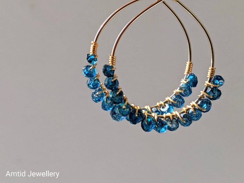 May include: Gold hoop earrings with blue gemstone beads. The earrings are made of wire and have a delicate, bohemian style.