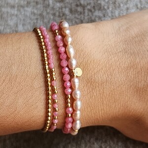 Puede incluir: Un conjunto de tres pulseras en tonos rosa y dorado. Una pulsera presenta peque&ntilde;as cuentas doradas, otra tiene cuentas de piedras preciosas rosas, y la tercera combina piedras rosas con perlas blancas. Se adjunta un peque&ntilde;o dije dorado.