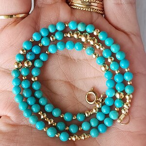 May include: A turquoise and gold beaded necklace with a clasp. The necklace is made of small, round turquoise beads and gold beads.