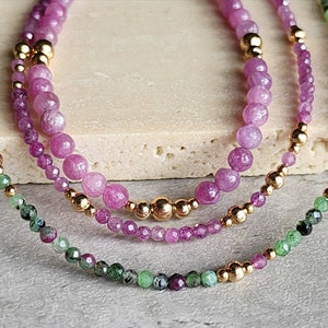 Puede incluir: Tres pulseras superpuestas con cuentas de piedras preciosas rosas y verdes y separadores de oro.