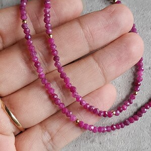 Pu&ograve; includere: Una delicata collana con piccole perline sfaccettate color rubino infilate insieme. La collana &egrave; impreziosita da piccole perline color oro. Il gioiello &egrave; esposto su uno sfondo neutro, evidenziando il colore vibrante delle pietre preziose.