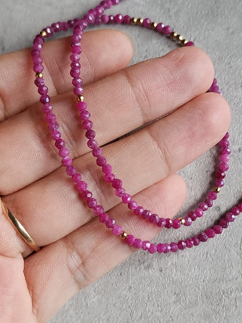 Pu&ograve; includere: Una delicata collana con piccole perline sfaccettate color rubino infilate insieme. La collana &egrave; impreziosita da piccole perline color oro. Il gioiello &egrave; esposto su uno sfondo neutro, evidenziando il colore vibrante delle pietre preziose.