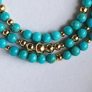 May include: A turquoise and gold beaded necklace with multiple strands. The necklace features round turquoise beads and small gold beads.