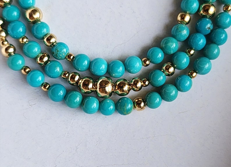 May include: A turquoise and gold beaded necklace with multiple strands. The necklace features round turquoise beads and small gold beads.