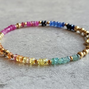 May include: A rainbow gemstone bracelet with gold beads and a clasp. The bracelet features pink, orange, yellow, green, blue, and purple gemstones.