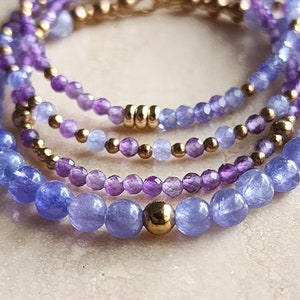 May include: A layered bracelet with amethyst and blue topaz beads, separated by gold beads.