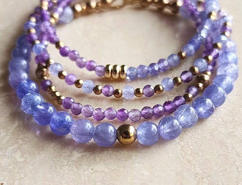 May include: A layered bracelet with amethyst and blue topaz beads, separated by gold beads.