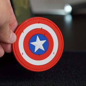 Könnte beinhalten: Ein runder roter, weißer und blauer Patch mit einem weißen Stern in der Mitte. Der Patch hat einen genähten Rand und scheint aus Stoff zu sein.