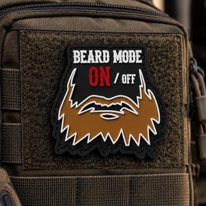 Könnte beinhalten: Ein schwarzer taktischer Aufnäher mit einer braunen Bartgrafik und weißen Umrandungen. Der Text lautet BEARD MODE ON / OFF, wobei das Wort ON in Rot gehalten ist. Der Aufnäher ist mit einem Klettverschluss an einer olivgrünen Tasche befestigt.