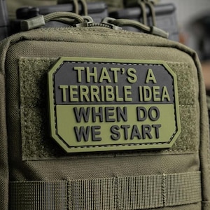 May include: An olive green tactical pouch featuring a rectangular morale patch with black raised lettering that reads, "THAT'S A TERRIBLE IDEA WHEN DO WE START." The pouch is constructed from durable fabric with integrated webbing straps and zip closures.