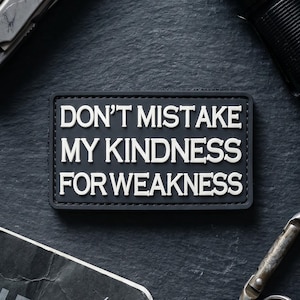 Op de afbeelding: Een rechthoekige zwarte patch met verhoogde witte letters die DON'T MISTAKE MY KINDNESS FOR WEAKNESS lezen. De patch heeft een strakke, gegoten rand en wordt gepresenteerd als een op zichzelf staand item met een matte afwerking en contrastrijke tekst.