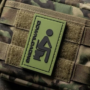 May include: A rectangular tactical pouch featuring a camouflage pattern in shades of green, brown, and black. A rectangular olive green morale patch is attached to the front, displaying a black graphic of a person on a toilet with the text DOWNLOADING.