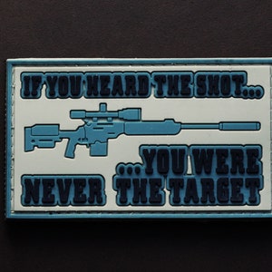 May include: A rectangular patch with a blue sniper rifle graphic and the text "IF YOU HEARD THE SHOT... YOU WERE NEVER THE TARGET" in white and blue. The patch has a white background and a blue border.