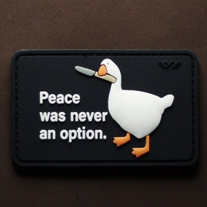 Könnte beinhalten: Ein schwarzer Patch mit weißem Text, der "Peace was never an option." lautet. Eine weiße Gans mit orangefarbenen Füßen hält ein Messer in ihrem Schnabel. Die Gans blickt nach rechts.
