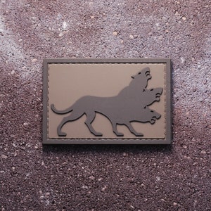 Può includere: Una toppa marrone con una silhouette nera di un cane a tre teste.