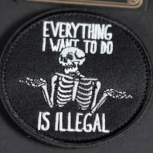 Op de afbeelding: Een ronde, zwart geborduurde patch met een wit skelet dat de armen omhoog houdt in een schouderophalend gebaar. De tekst "EVERYTHING I WANT TO DO IS ILLEGAL" is in witte hoofdletters boven en onder het skeletfiguur geborduurd.