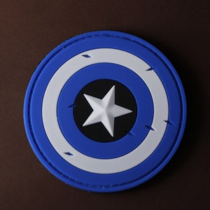 May include: Blue and white circular patch with a white star on a black background. The patch has a stitched edge.