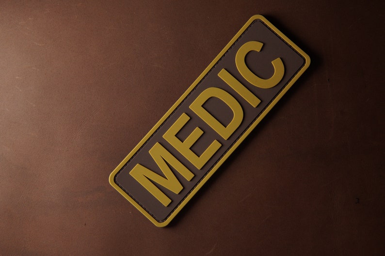 Pu&ograve; includere: Un cerotto rettangolare marrone con un bordo giallo e la parola "MEDIC" scritta in lettere gialle.