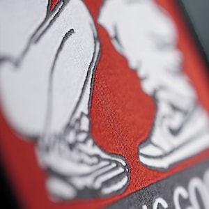 Può includere: Una toppa ricamata rossa e nera con due gambe bianche in scarpe da ginnastica e il testo "Feeling Good" in nero.