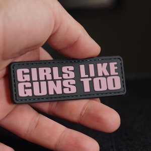 Könnte beinhalten: Schwarzer Patch mit rosa Schriftzug "Girls Like Guns Too".