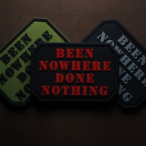 Könnte beinhalten: Drei schwarze und grüne Stoff-Patches mit dem Text "Been Nowhere Done Nothing" in roten und weißen Buchstaben.