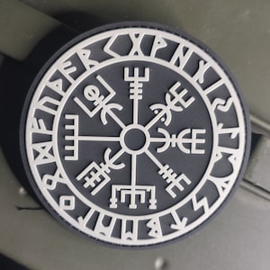 May include: A black and white compass with a white circle in the centre and a white ring around the outside. The ring has runes written around it.