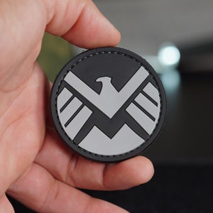 Peut inclure: Un écusson brodé noir et gris avec un motif d'aigle stylisé. L'écusson a une bordure noire cousue.