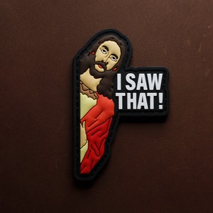 Könnte beinhalten: Ein schwarz-weißes Patch mit einem Cartoon-Bild von Jesus, der um eine Ecke lugt. Der Text "I SAW THAT!" ist in Weiß auf dem Patch gedruckt.