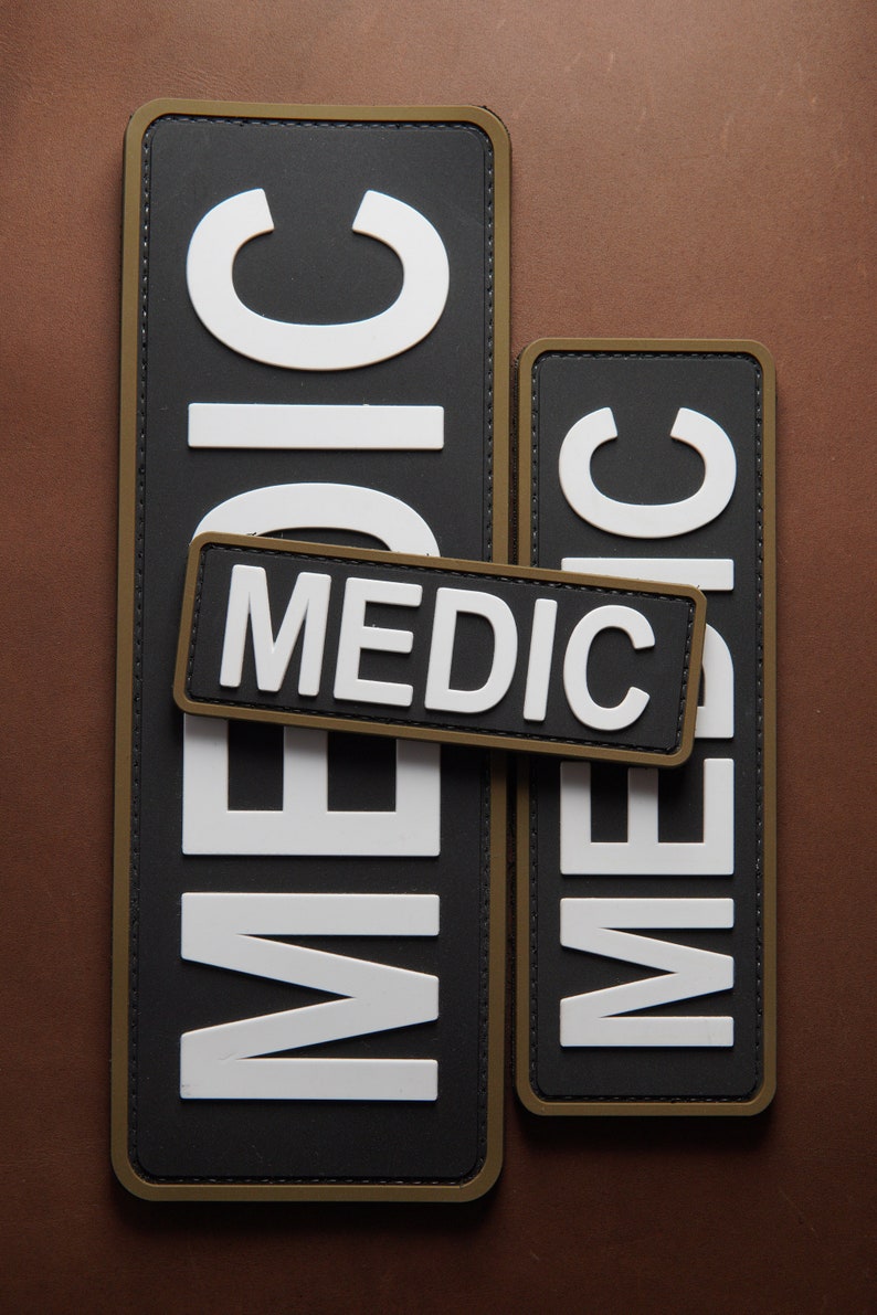 Pu&ograve; includere: Due patch "MEDIC" neri e bianchi con cuciture verde oliva. I patch sono rettangolari e hanno un design in rilievo testurizzato.