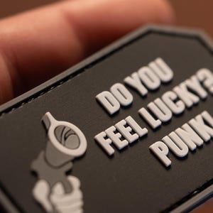 May include: Black and white patch with a gun and the text "Do you feel lucky punk?"