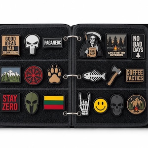 May include: A black binder with three metal rings containing a collection of various rectangular, circular, and shaped morale patches. The patches feature diverse designs including skulls, nature scenes, text, flags, and symbols attached to a black fabric.