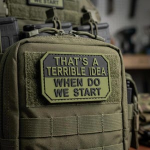 May include: An olive green tactical pouch featuring a rectangular morale patch with raised black lettering that reads, THAT'S A TERRIBLE IDEA WHEN DO WE START. The pouch is constructed from durable fabric with integrated webbing and zipper closures.