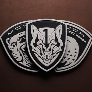 Peut inclure: Trois patchs brodés en noir et blanc. Le patch central représente une tête de loup avec le chiffre "1" sur son front. Le patch de gauche représente une tête d'ours. Le patch de droite représente une étoile et le texte "Project Honor".